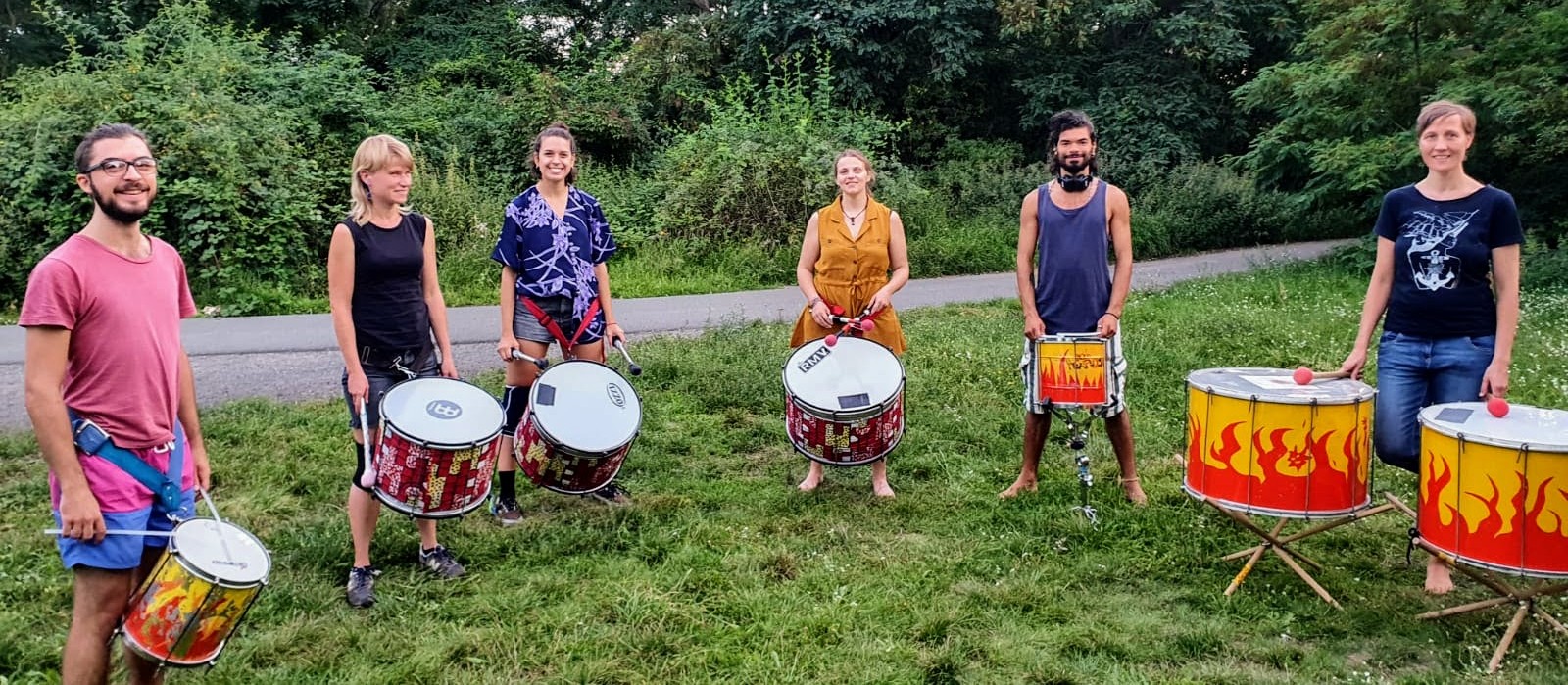 group of six percussionists with their instruments looking at the camera standing in the grass